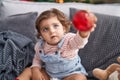 Adorable hispanic girl holding ball decoration sitting on sofa by christmas tree at home Royalty Free Stock Photo