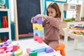 Adorable hispanic girl playing with construction blocks sitting on chair at kindergarten