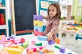 Adorable hispanic girl playing with construction blocks sitting on chair at kindergarten