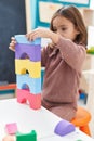 Adorable hispanic girl playing with construction blocks sitting on chair at kindergarten