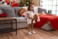 Adorable hispanic girl playing with horse toy standing by christmas tree at home Royalty Free Stock Photo