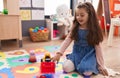 Adorable hispanic girl playing with tractor toy sitting on floor at kindergarten Royalty Free Stock Photo