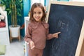 Adorable hispanic girl preschool student smiling confident writing name on blackboard at kindergarten