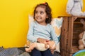 Adorable hispanic girl sitting on sofa playing with baby doll at home Royalty Free Stock Photo