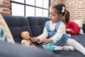 Adorable hispanic girl sitting on sofa playing with baby doll at home Royalty Free Stock Photo