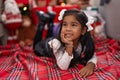 Adorable hispanic girl smiling confident lying on floor by christmas tree at home Royalty Free Stock Photo