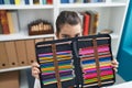 Adorable hispanic girl student sitting on table covering face with pencils case at classroom Royalty Free Stock Photo