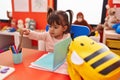 Adorable hispanic girl student sitting on table holding color pencils at kindergarten Royalty Free Stock Photo