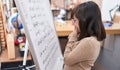 Adorable hispanic girl student standing by chalkboard solving maths exercise at classroom