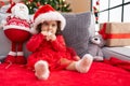 Adorable hispanic girl sucking stair decoration sitting on sofa by christmas tree at home Royalty Free Stock Photo