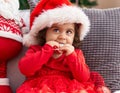 Adorable hispanic girl sucking stair decoration sitting on sofa by christmas tree at home Royalty Free Stock Photo