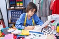 Adorable hispanic girl tailor drawing on notebook at clothing factory