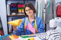 Adorable hispanic girl tailor smiling confident holding cloths at clothing factory