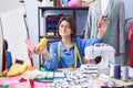 Adorable hispanic girl tailor smiling confident holding scissors and thread at clothing factory