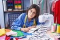 Adorable hispanic girl tailor writing on notebook at clothing factory