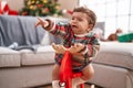 Adorable hispanic toddler crying and playing with reindeer rocking by christmas tree at home