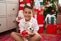 Adorable hispanic toddler hugging teddy bear sitting on floor by christmas gifts at home Royalty Free Stock Photo