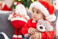 Adorable hispanic toddler hugging teddy bear sitting on sofa by christmas tree at home Royalty Free Stock Photo