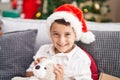 Adorable hispanic toddler hugging teddy bear sitting on sofa by christmas tree at home Royalty Free Stock Photo