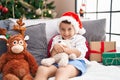 Adorable hispanic toddler hugging teddy bear sitting on sofa by christmas tree at home Royalty Free Stock Photo