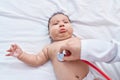 Adorable hispanic toddler lying on bed having chest auscultation at bedroom Royalty Free Stock Photo