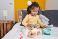 Adorable hispanic toddler playing with baby doll sitting on bed at bedroom Royalty Free Stock Photo