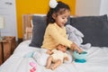 Adorable hispanic toddler playing with baby doll sitting on bed at bedroom Royalty Free Stock Photo