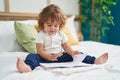 Adorable hispanic toddler reading book sitting on bed at bedroom Royalty Free Stock Photo