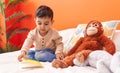 Adorable hispanic toddler reading book sitting on bed at bedroom Royalty Free Stock Photo