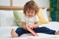 Adorable hispanic toddler reading book sitting on bed at bedroom Royalty Free Stock Photo