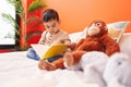 Adorable hispanic toddler reading book sitting on bed at bedroom Royalty Free Stock Photo