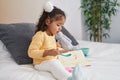 Adorable hispanic toddler sitting on bed reading book at bedroom Royalty Free Stock Photo