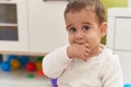 Adorable hispanic toddler sitting on floor sucking hand at kindergarten Royalty Free Stock Photo