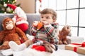 Adorable hispanic toddler sucking doll sitting on sofa by christmas tree at home