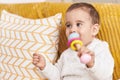 Adorable hispanic toddler sucking toy sitting on sofa at home