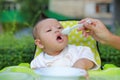 Adorable infant baby boy sitting in the chair and eating food for the first time. Hand of mother feeding food into baby mouth by Royalty Free Stock Photo