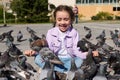 Adorable Joyful Little Child Girl Sitting In Lotus Pose And Feeding Flock Of Flying Pigeons And Birds In The Park Square