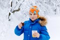 Adorable kid boy drinking hot chocolate and eating brownie cake in winter forest. Happy healthy child with cup of Royalty Free Stock Photo