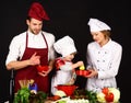 Adorable kid in chef hat with her parents. Mother and father teaching boy how to cook. Concept of friendly family  mutual Royalty Free Stock Photo