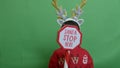 Adorable kid with double headband christmas deer antlers showing sign santa stop here. Isolated on green