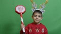 Adorable kid with double headband christmas deer antlers showing sign santa stop here. Isolated on green