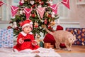 An adorable kid dressed as Santa Claus plays near a decorated Christmas tree in the living room. A cat walks around the gifts Royalty Free Stock Photo