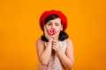 Adorable kid eating candy with pleasure. Studio shot of brunette little girl with lollipop isolated on yellow background