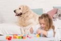 adorable kid playing with educational cubes, golden retriever dog lying on bed