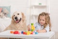 adorable kid playing with educational cubes, golden retriever sitting near table