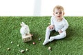Kid sitting on green grass near wooden calendar with 28 April date, decorative rabbit and colorful Easter eggs isolated Royalty Free Stock Photo