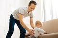 Adorable kind father helping his baby to stand near the sofa