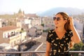 Adorable lady with long brown hair posing on terrace on blur city background. Outdoor portrait of joyful girl with shades and