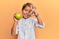 Adorable latin kid holding green apple doing ok sign with fingers, smiling friendly gesturing excellent symbol Royalty Free Stock Photo