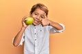 Adorable latin kid holding green apple smiling happy and positive, thumb up doing excellent and approval sign Royalty Free Stock Photo